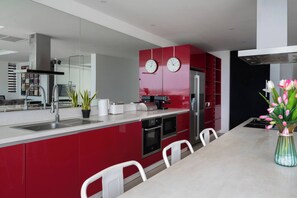 A modern kitchen with red cabinetry, stainless steel appliances, and a dining area with white chairs. - Central Villa With Mountain & sea View (Koh Samui)