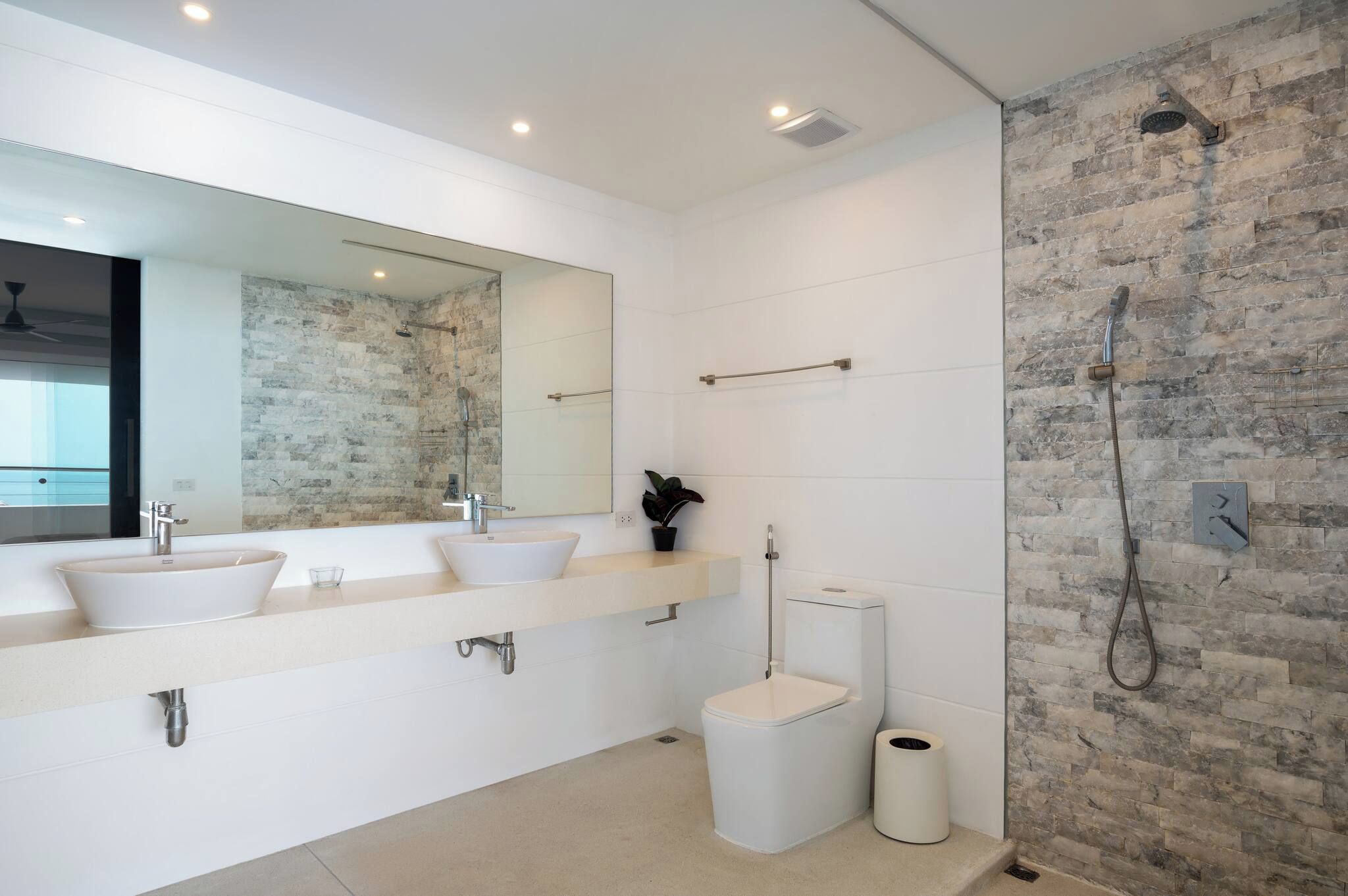 A modern bathroom with a large mirror, two sinks, a toilet, and a shower.