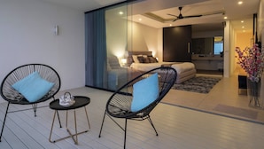A modern living space with a glass partition, a sofa, a bed, and two wicker chairs with cushions. - Central Villa With Mountain & sea View (Koh Samui)