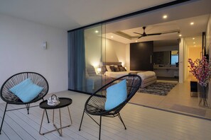 Un espacio habitable moderno con un separador de vidrio, un sofá, una cama y dos sillones de mimbre con cojines.