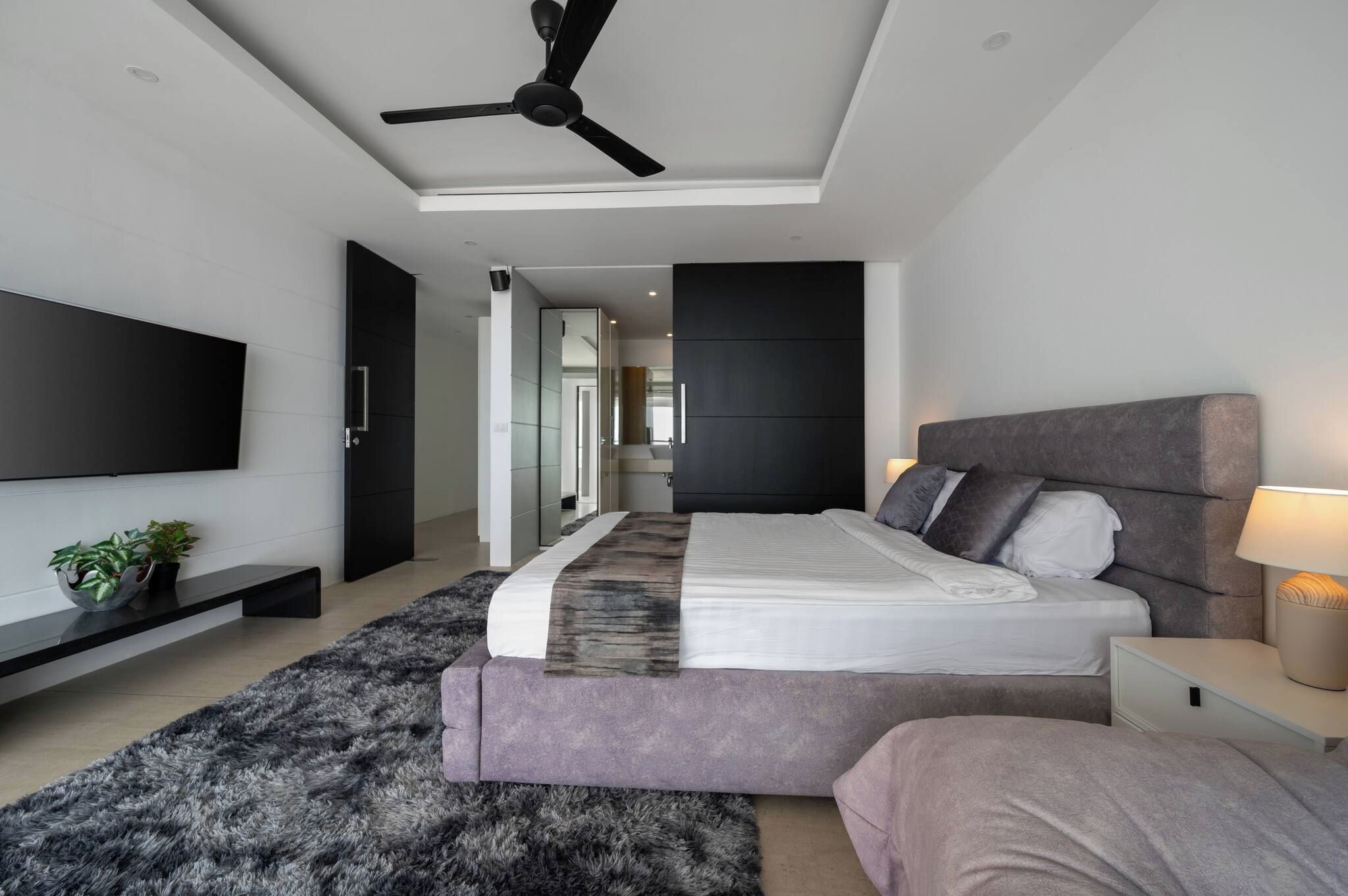 Quarto moderno com cama, mesas de cabeceira, televisão e ventoinha de teto.