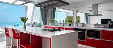 A modern kitchen with a central island, red cabinetry, and a view of the ocean.