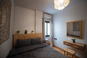 Ein Schlafzimmer mit einem Bett, einem Holz-Kopfstück, einem Nachttisch, einem Spiegel und einem Fenster mit Vorhängen.