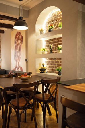 A dining area with a brick wall, wooden chairs, a table with a bowl of fruit, and a hanging light fixture. - Chic 2-Bedroom Loft - Walk to Egyptian Museum, Tahrir Sq. & Nile (Cairo Governorate)