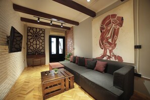 A modern living room with a herringbone floor, a sectional sofa, a wooden coffee table, and a large abstract painting on the wall. - Chic 2-Bedroom Loft - Walk to Egyptian Museum, Tahrir Sq. & Nile (Cairo Governorate)
