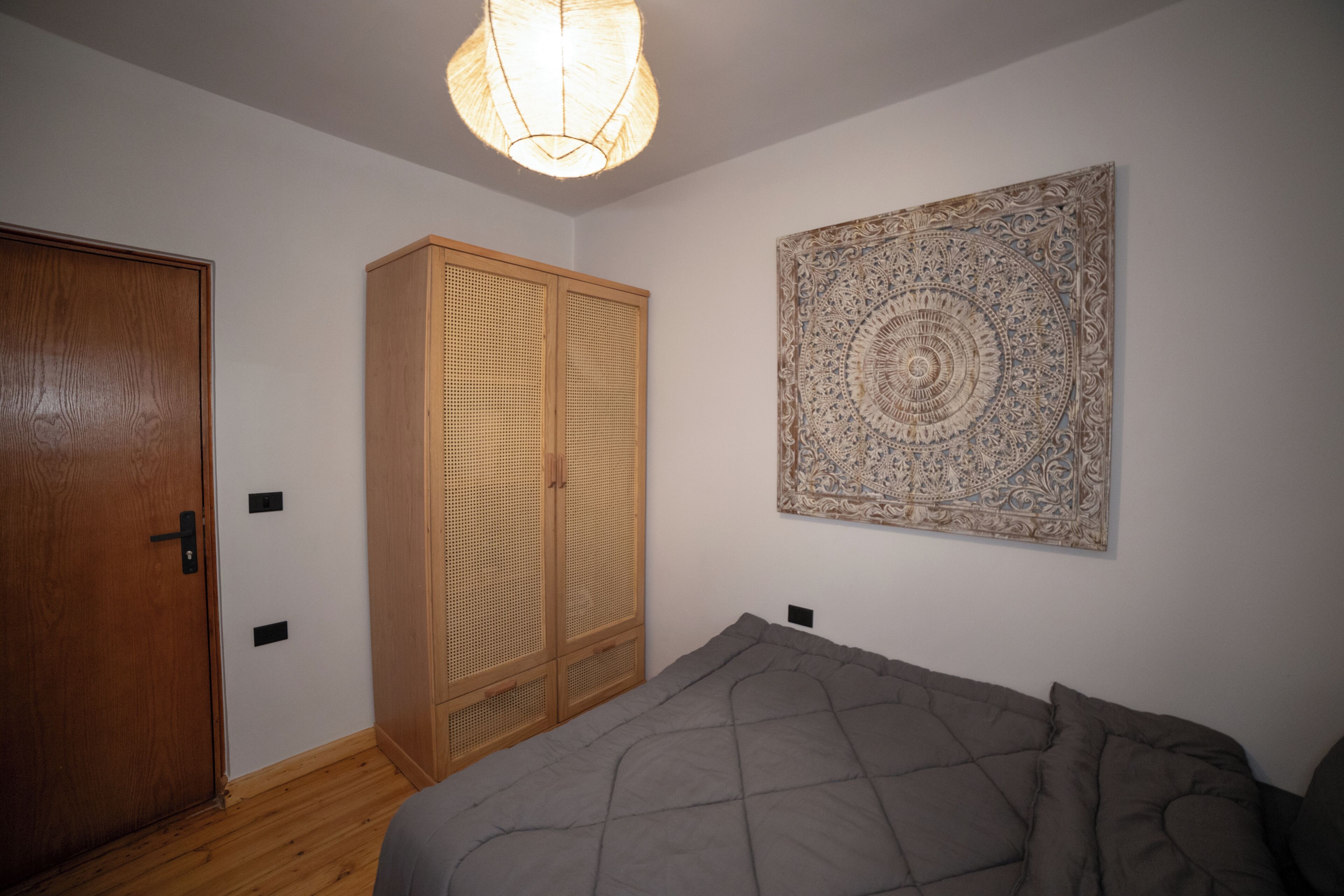 A bedroom with a bed, a wooden wardrobe, a door, and a wall-mounted tapestry.