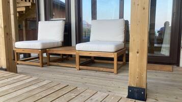 Una terraza de madera con dos sillas blancas acolchadas y una mesa de madera.