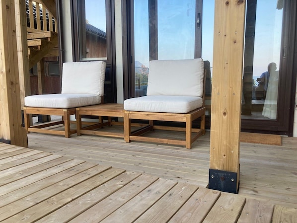 A wooden deck with two white cushioned chairs and a wooden table.