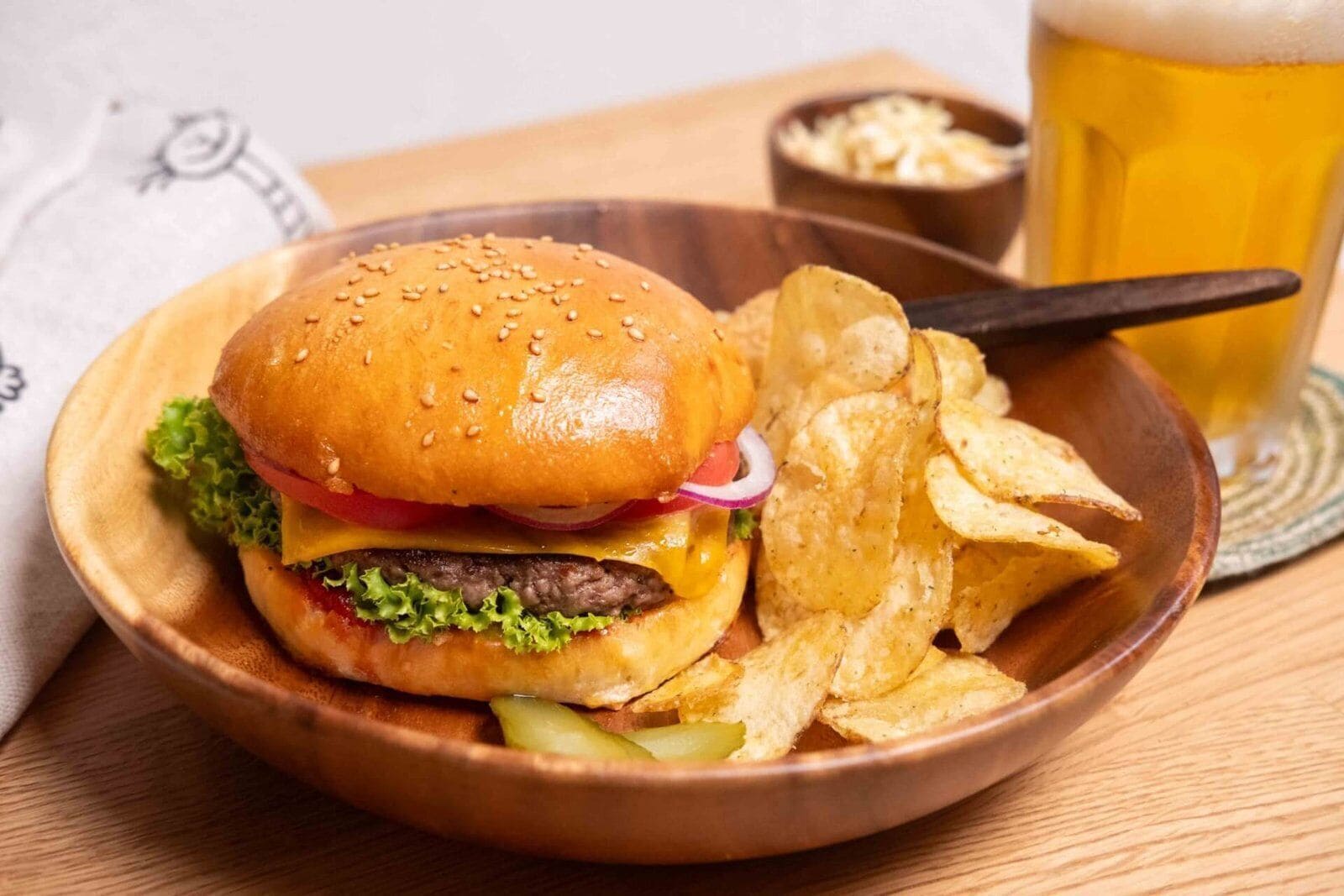 Una comida que incluye una hamburguesa, papas fritas y una jarra de cerveza sobre una mesa de madera.