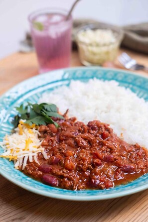 A plate with rice, beans, and shredded cheese, accompanied by a drink and a small bowl of sauce.