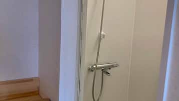 A small, enclosed shower area with a handheld showerhead and a wall-mounted faucet.