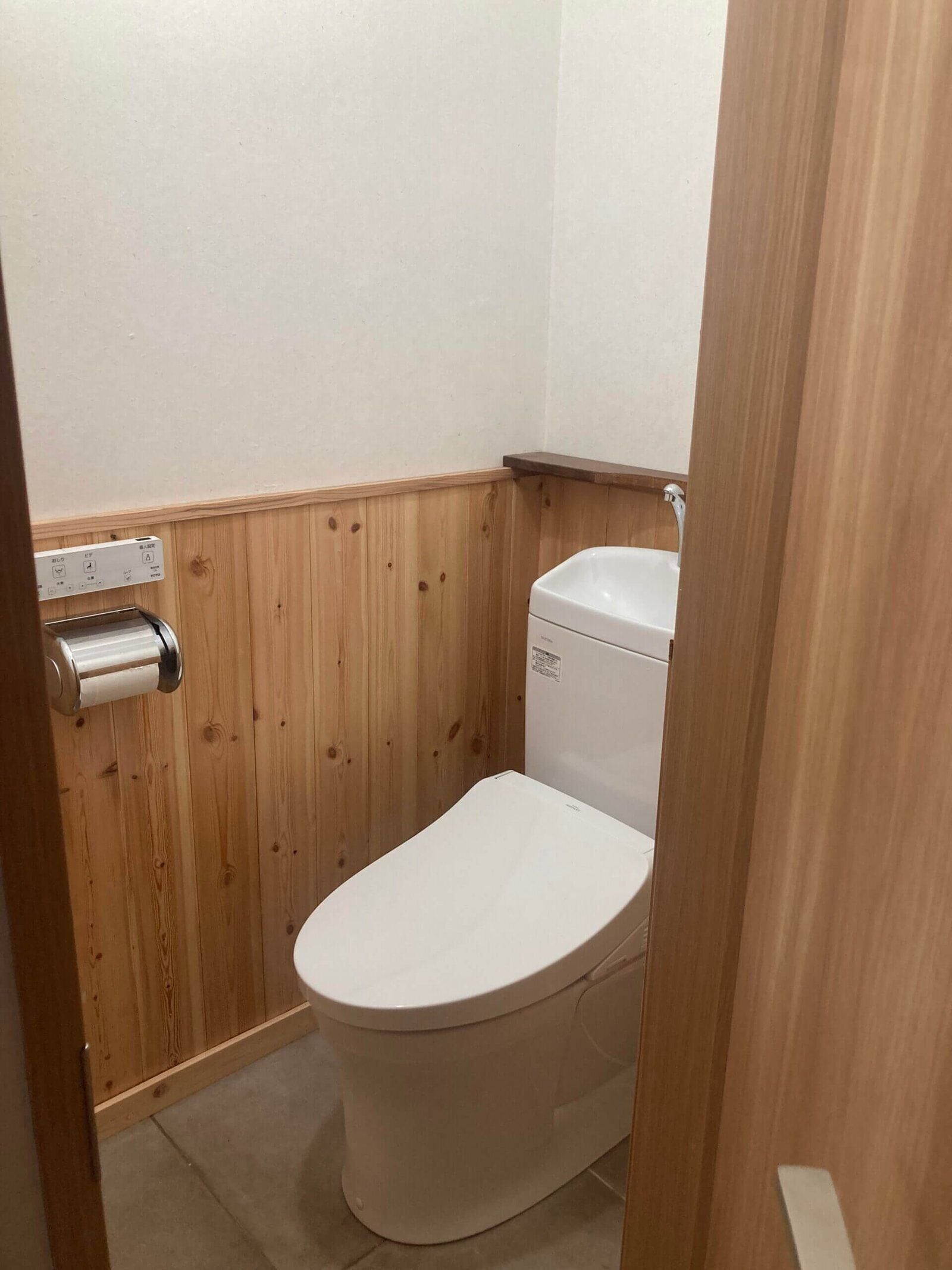 A small, compact bathroom with a wooden panel wall, a white toilet, and a toilet paper holder.