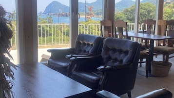 A room with a view of mountains and a body of water. There are leather chairs and a wooden table.