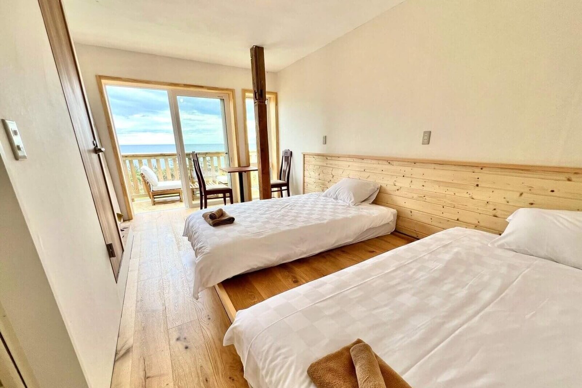 A hotel room with two beds, a wooden headboard, and a balcony with chairs.