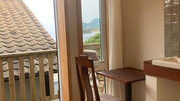 A room with a wooden table, a chair, a window with curtains, a view of the sea, and a tiled wall.