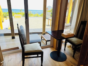A room with a wooden floor, a sofa, a table, and a view of the sea through large windows.