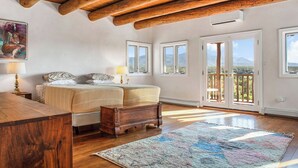 Ein Schlafzimmer mit Holzboden, einem Bett mit Kopfteil, einem Nachttisch, einer Lampe und einem Blick ins Freie.
