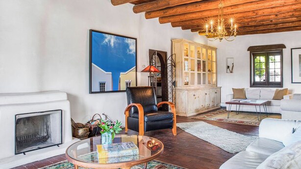 Ein Wohnzimmer mit Kamin, einem Glastisch, einem Ledersessel, einem weißen Sofa und einer Holzbalkendecke.