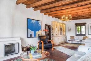 A living room with a fireplace, a glass coffee table, a leather armchair, a white sofa, and a wooden ceiling.