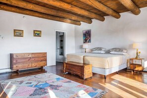 A bedroom with a wooden ceiling, a bed with a patterned bedspread, a wooden dresser, a rug, and a nightstand with a lamp.