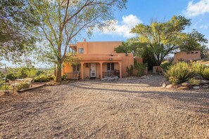 A single-story house with a gravel driveway, surrounded by trees and desert plants. - 1795 Adobe, Dog Friendly · High Road to Taos (Ranchos de Taos)
