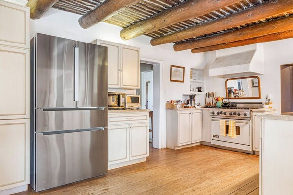A kitchen with a stainless steel refrigerator, white cabinets, a wooden ceiling, and a vintage stove.