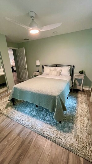 A bedroom with a bed, a nightstand, a lamp, a ceiling fan, and a door leading to another room. -  Newly remodeled Serene 3-bedroom home in Crescent City (Crescent City)