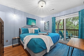 A bedroom with a bed, a bedside table, a window with curtains, and a view of trees outside.