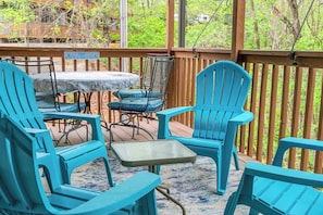 A covered outdoor seating area with turquoise chairs and a table, surrounded by a wooden deck and a railing.