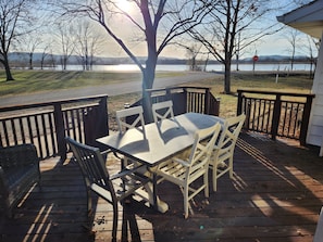 A wooden deck with a table and chairs, overlooking a body of water and a distant mountain range. - Charming Waterfront Retreat on the Mississippi River (Buffalo City)