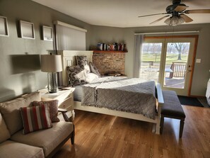 A bedroom with a bed, a bench, a nightstand, a lamp, a bookshelf, and a view of the outdoors through a door. - Charming Waterfront Retreat on the Mississippi River (Buffalo City)