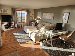 A living room with a sofa, a TV, a desk with a computer, and a window with a view. - Charming Waterfront Retreat on the Mississippi River (Buffalo City)