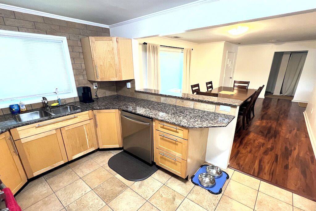 A kitchen with wooden cabinets, a dishwasher, granite countertops, and a dining area with a table and chairs.