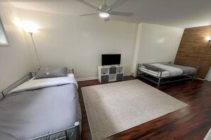Een kamer met twee bedden, een tv-meubel en een plafondventilator.