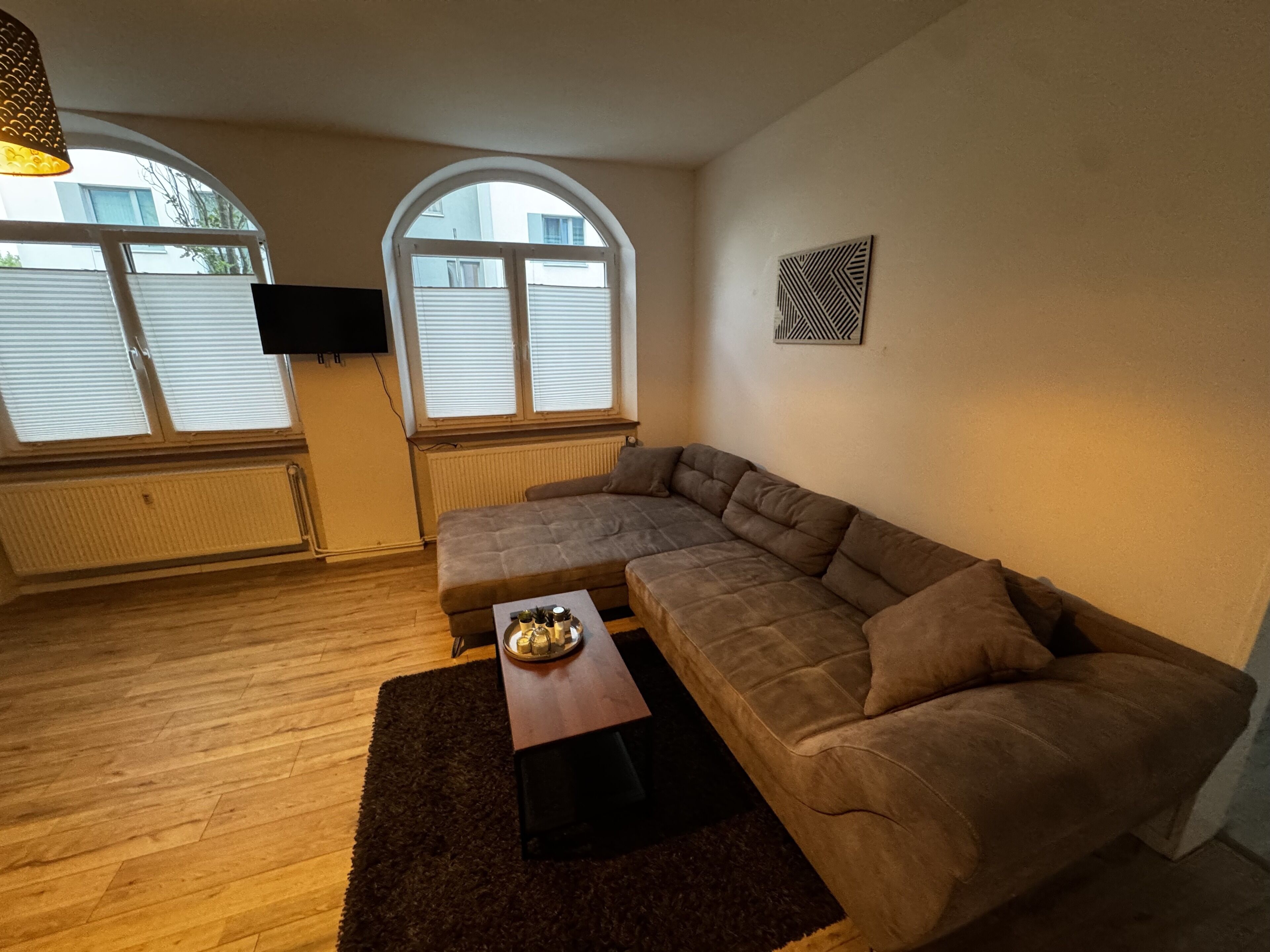 Ein Wohnzimmer mit einer Eckcouch, einem Couchtisch und einem an der Wand befestigten Fernseher.