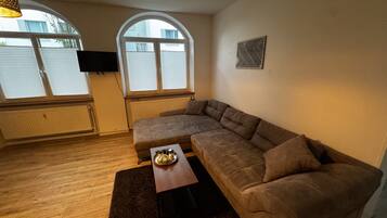 Ein Wohnzimmer mit einer Eckcouch, einem Couchtisch und einem an der Wand befestigten Fernseher.