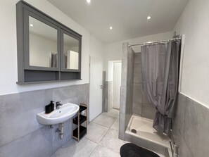 Ein modernes Badezimmer mit Waschbecken, Spiegel, Dusche mit Glastür und grauen Fliesen.