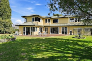 A two-story house with a patio, a lawn, and a fence. - Shore Haven - Lakefront, Spa Pool, Sleeps 8 (Rotorua)