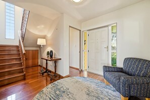 A spacious room with a wooden staircase, a round rug, a patterned sofa, and a table with decorative items. - Shore Haven - Lakefront, Spa Pool, Sleeps 8 (Rotorua)