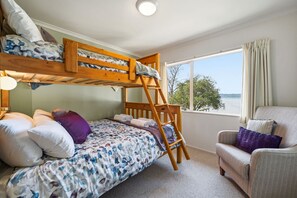 A room with a bunk bed, a chair, and a window with a view. - Shore Haven - Lakefront, Spa Pool, Sleeps 8 (Rotorua)