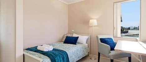 A bedroom with a single bed, a chair, a desk, and a window.
