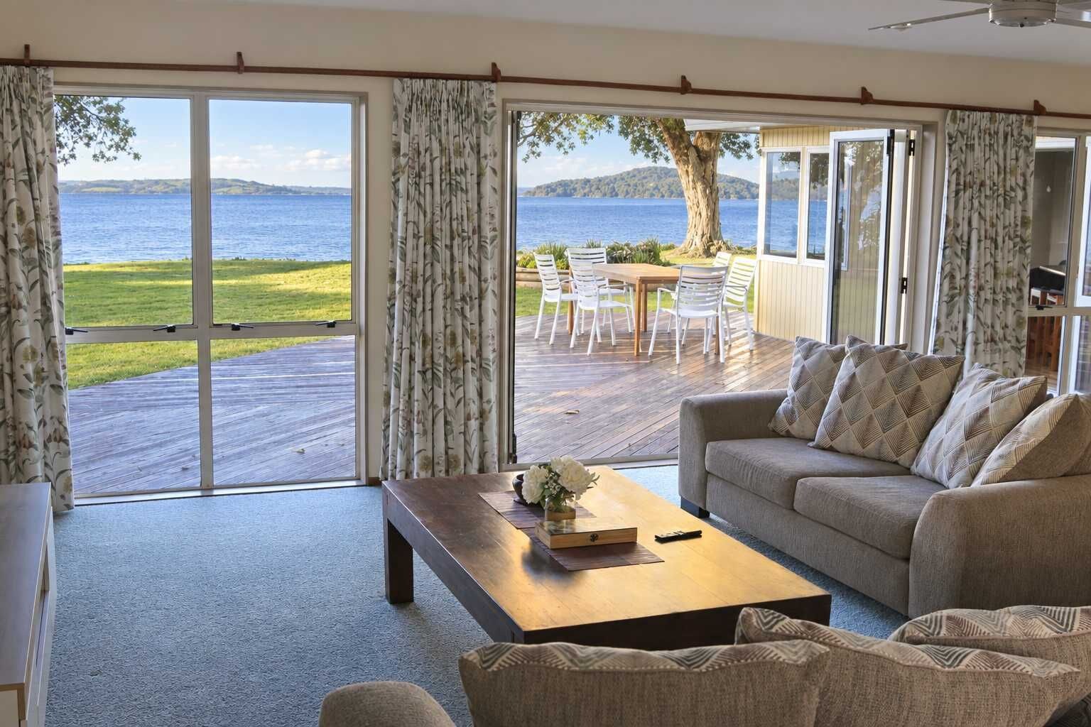 A living room with a large sliding glass door leading to an outdoor deck with a view of the sea and hills.