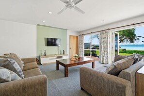 A modern living room with a flat-screen TV, a wooden coffee table, and a large sofa. - Shore Haven - Lakefront, Spa Pool, Sleeps 8 (Rotorua)