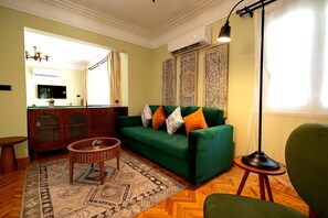 A living room with a green sofa, patterned rug, and a television on the wall. - Heliopolis 2 Bedrooms Apartments with Huge Patio - 10 Minutes to Airport (Cairo Governorate)