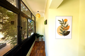 Ein Flur mit Holzboden, einem Fenster mit Jalousien, einer Pendelleuchte und einem gerahmten abstrakten Kunstwerk an der Wand.