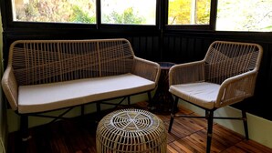 Una stanza con pavimento in legno, un divano, due poltrone e un poggiapiedi in vimini.