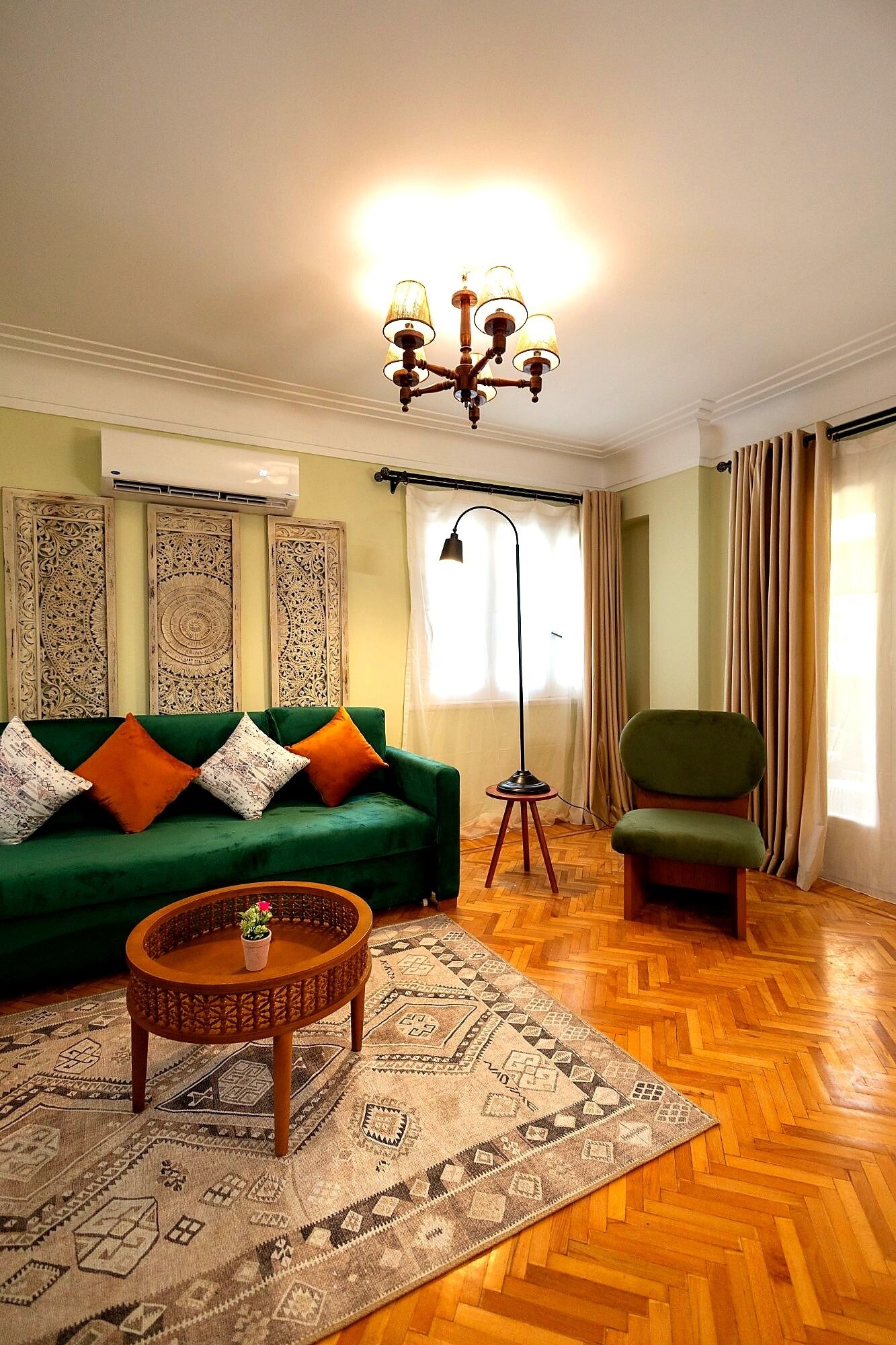 A living room with a green sofa, a wooden coffee table, a patterned rug, a floor lamp, and a chair.