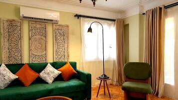 A living room with a green sofa, a wooden coffee table, a patterned rug, a floor lamp, and a chair.
