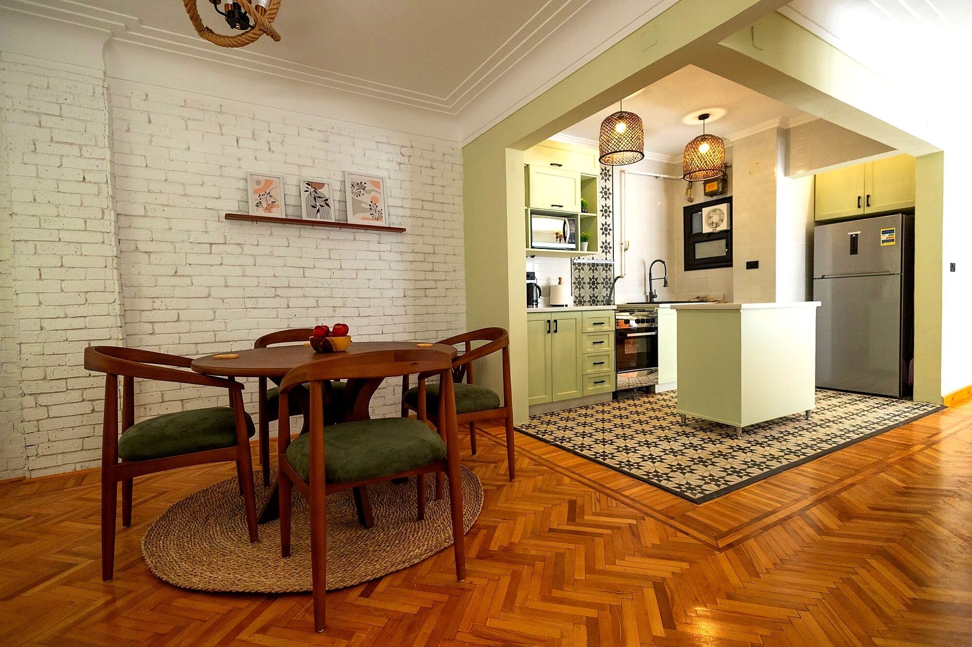 A dining area with a wooden table and chairs, a kitchen with a refrigerator and microwave, and a patterned floor.