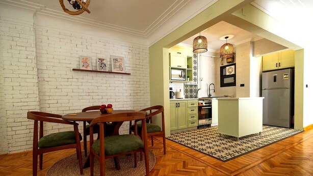Zona pranzo con tavolo e sedie in legno, cucina con frigorifero e forno a microonde, e pavimento decorato.